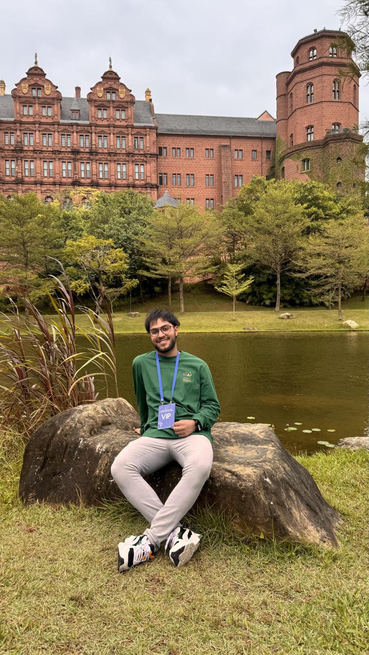 Omar Farouk sitting on a rock by a pond, with a red brick building behind